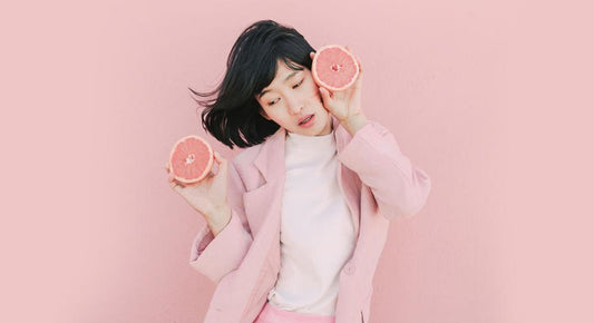 Asian woman wearing pink blazer and white tshirt holding two grapefruits 