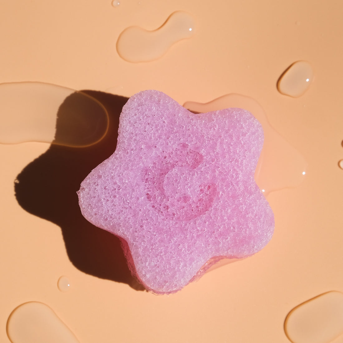 Clean Circle cherry blossom konjac facial sponge with water droplets surrounding it on orange background